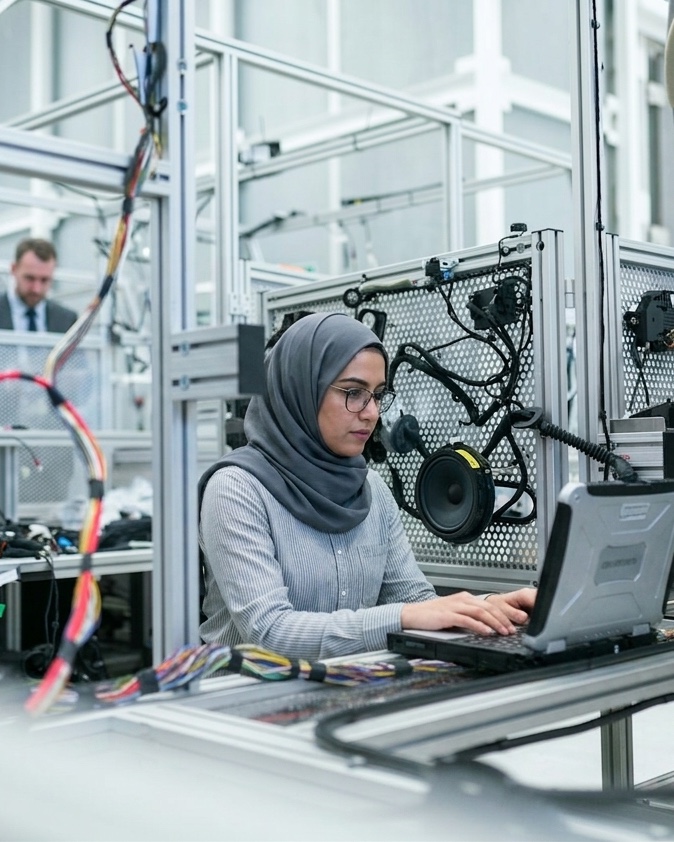 A Maseer-trained engineer in a hijab working on an industrial automation control system at a UAE technology workbench